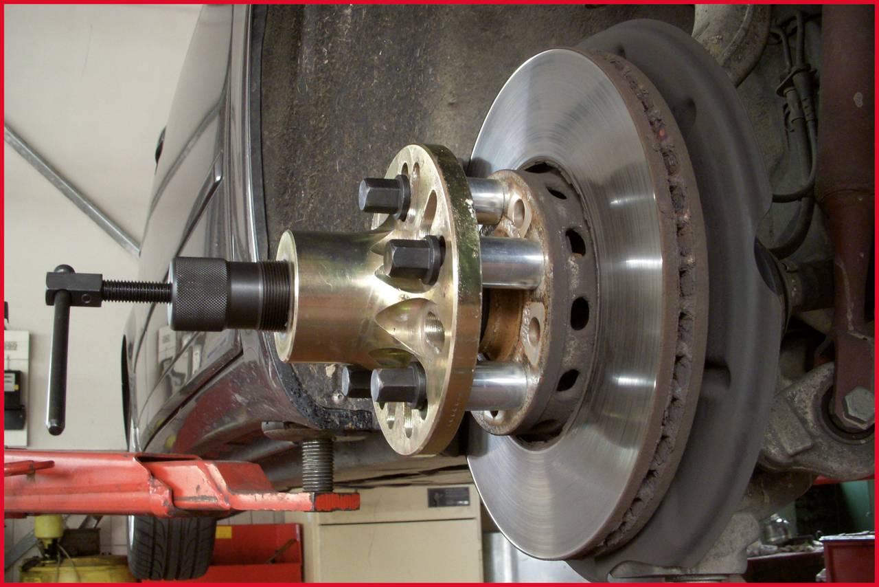 A brake disc of a car is being machined with a specialist tool. The vehicle is jacked up, with part of the underside visible.