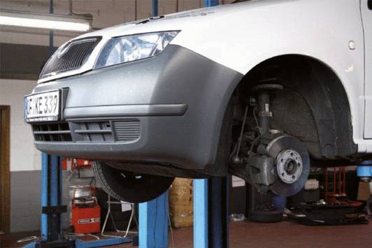 A car is raised on a vehicle lift, with the right front wheel removed, revealing the brake disc.