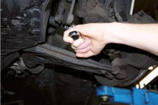A hand is holding a tool to inspect a car part underneath the vehicle.