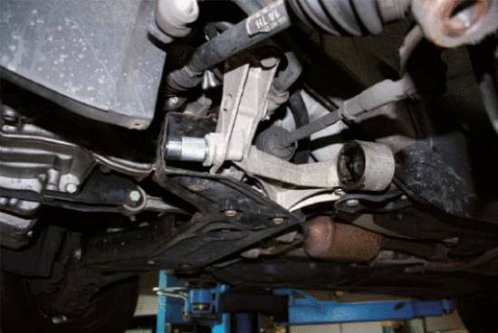 View from underneath a vehicle raised on a vehicle lift in a workshop, revealing details of the suspension and exhaust system.