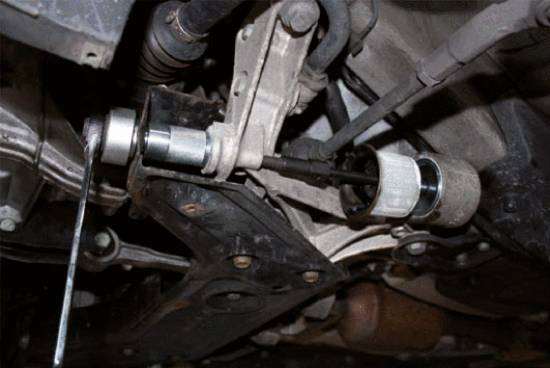 A mechanic is working underneath a car, using tools on a component in the chassis to carry out a repair.
