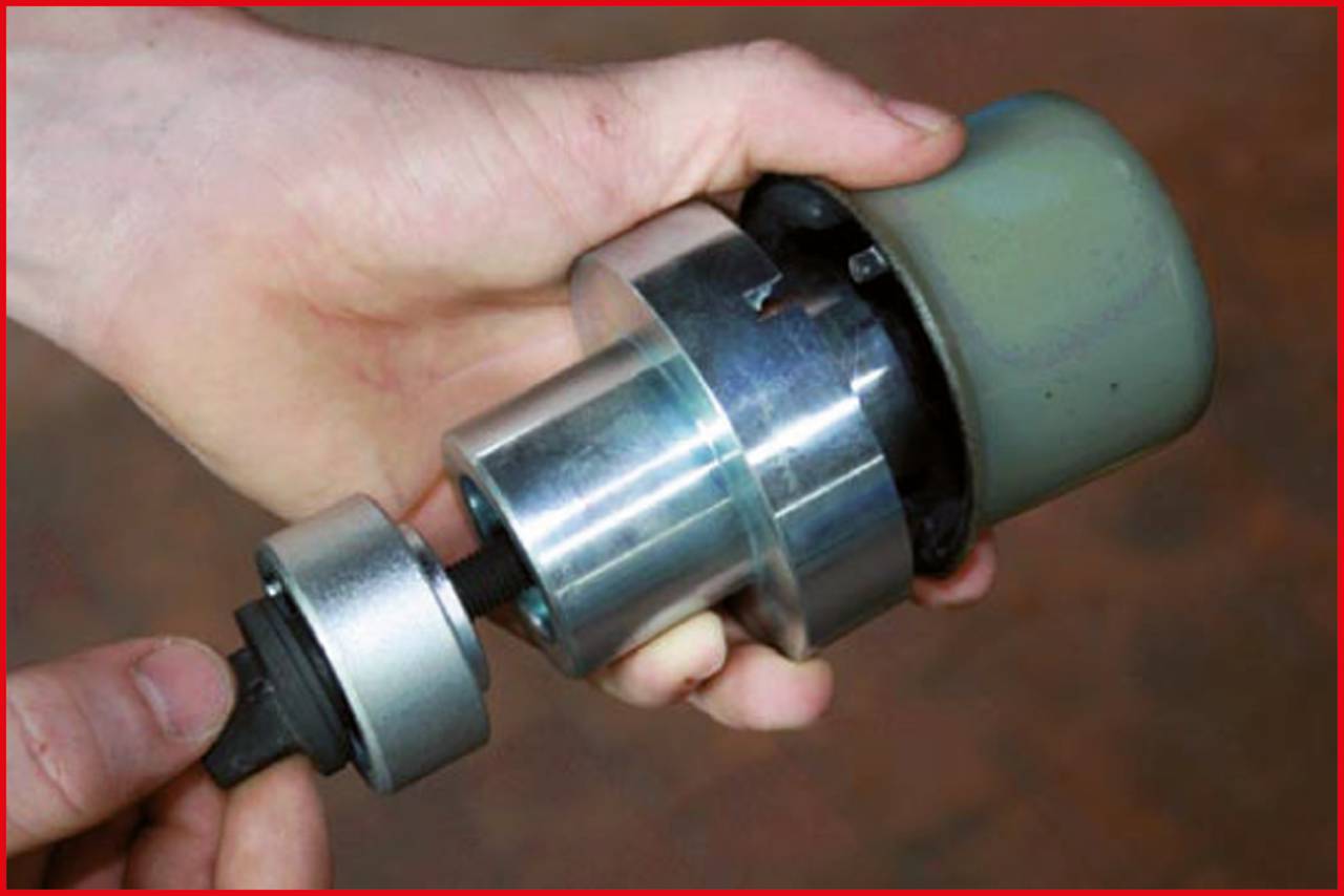 A hand is holding a cylindrical metal tool comprised of multiple components, likely used for assembly or repair.