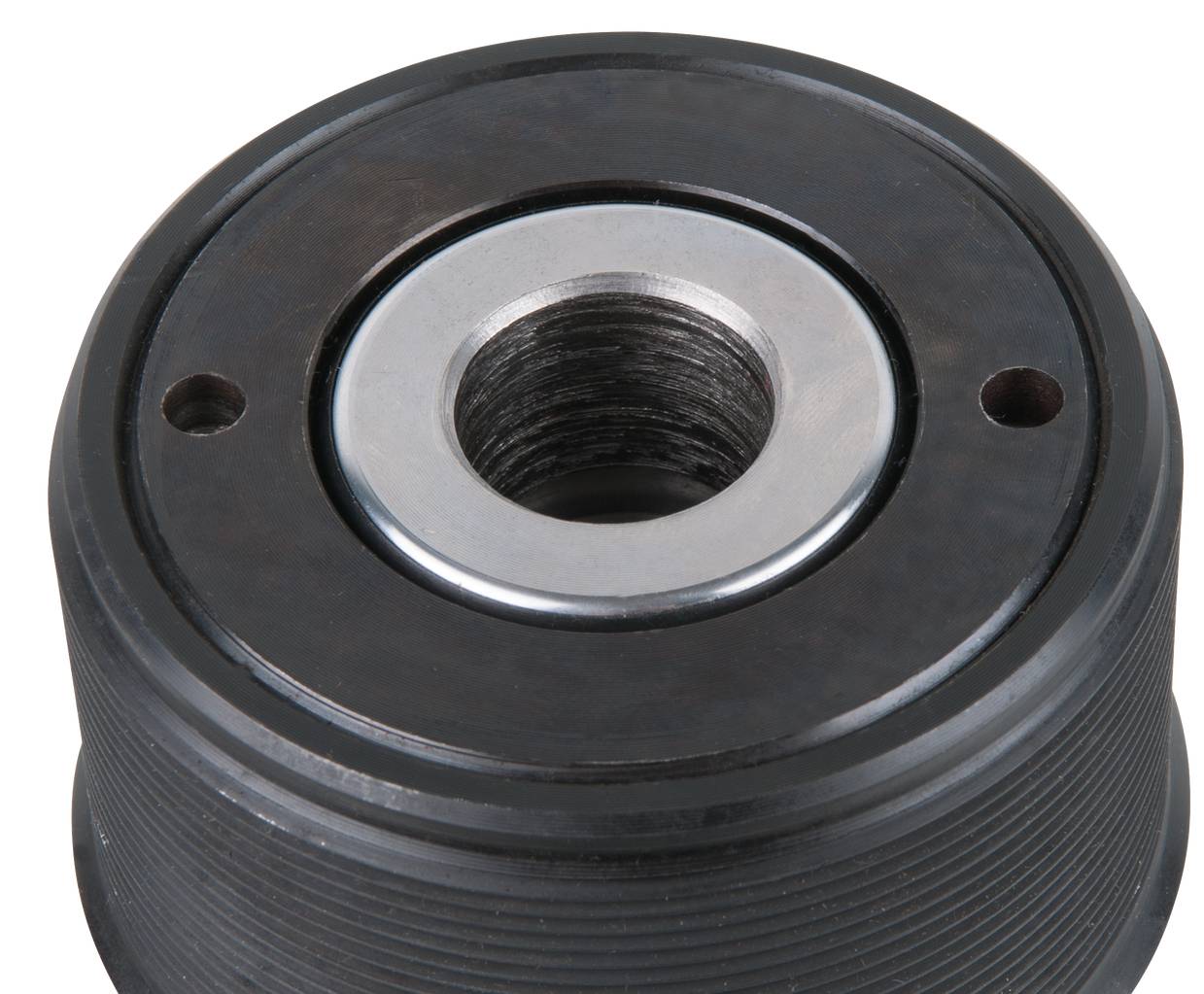 Black grey metal bearing with a central opening, surrounded by two smaller holes on a surface.