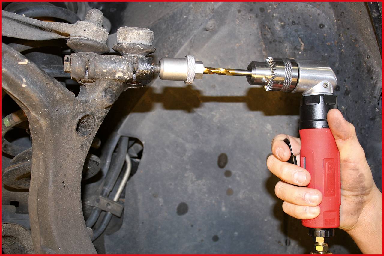 A person is using a red angle grinder to work on a metal part in a vehicle's chassis.