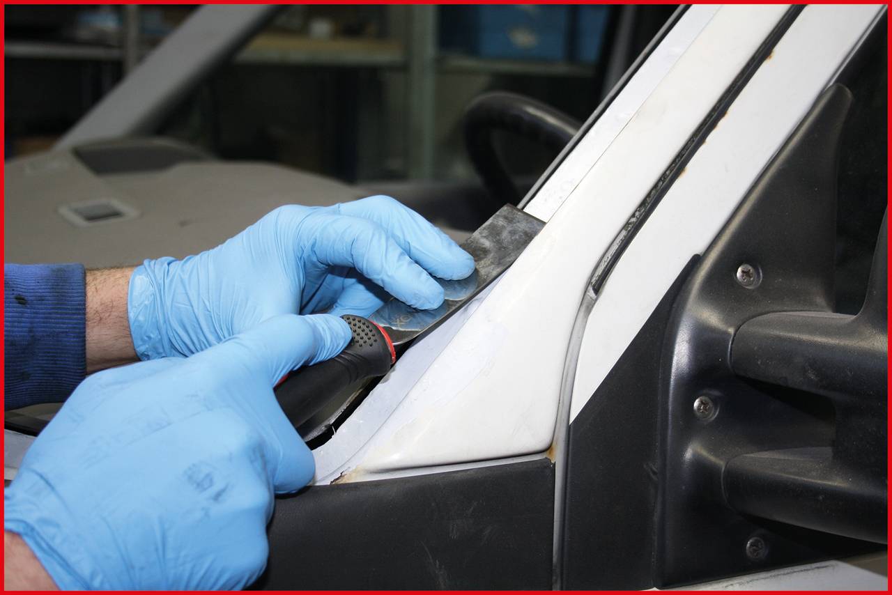 A person wearing blue gloves is working on a vehicle's bodywork with a grinding tool.