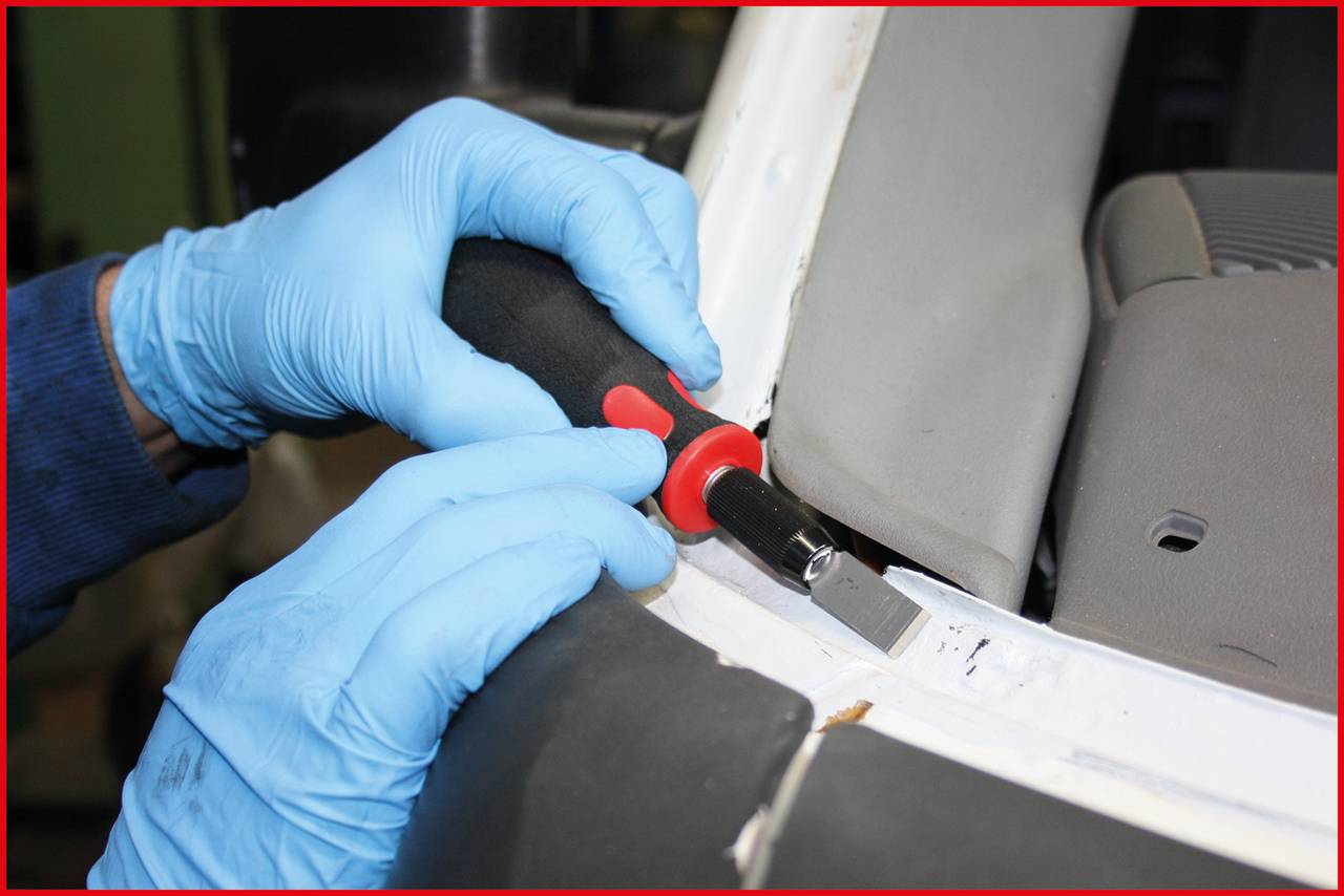A person is wearing blue gloves and using a specialist tool to carefully remove the interior trim of a car.