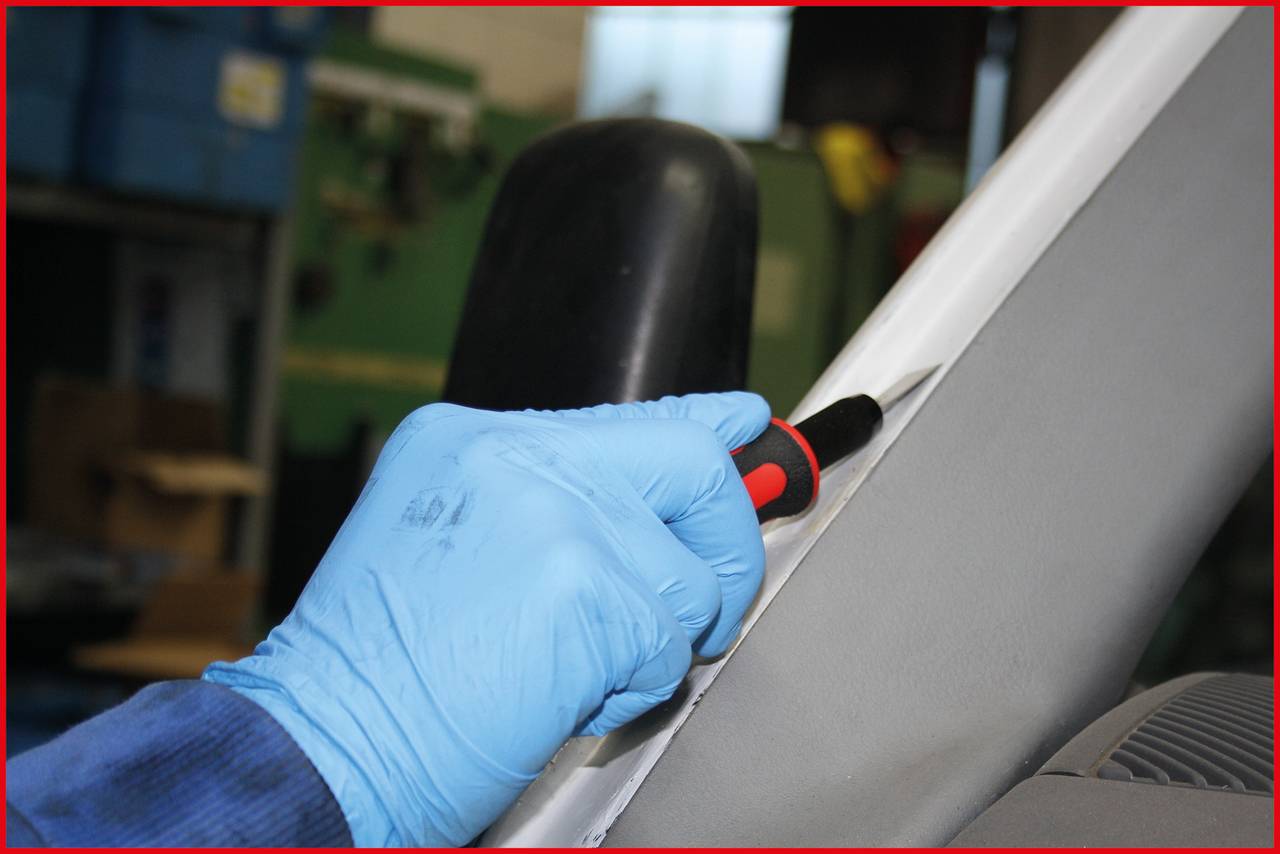 A person wearing blue protective gloves is using a screwdriver to work on a white object in a workshop.