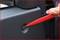 A hand is using a red plastic tool to carefully remove a small cap from the car door cover.