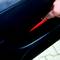 A person is holding a red object in a narrow gap of a car part. The focus is on the hand and the object.