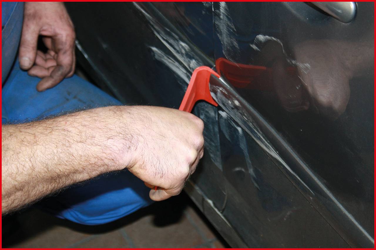 'A person removes dents from a car door with a red tool.'