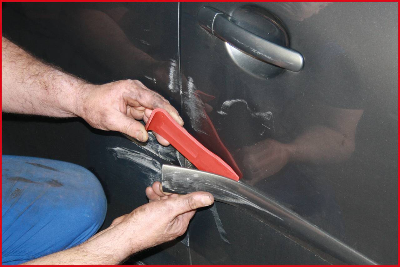 A person is polishing a car door using two polishing tools. The door has visible scratches that are being removed.