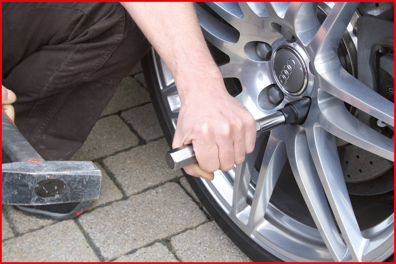 'Someone is changing a wheel on a car, using a wheel nut spanner. A hand and the car tyre are visible.'