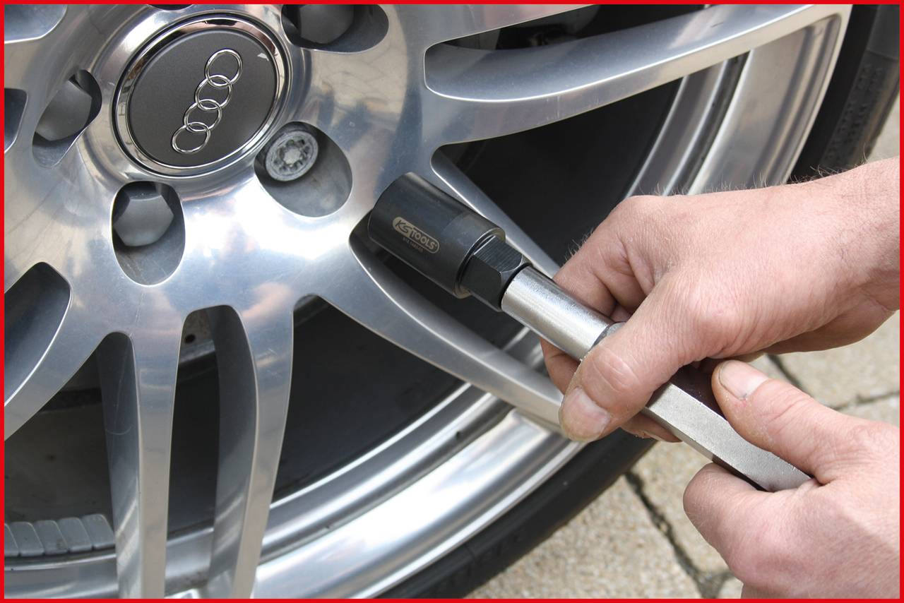 'Two hands are tightening a wheel nut on a car with a tool.'