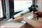 A person is sealing the edge of a window frame with a caulking gun.