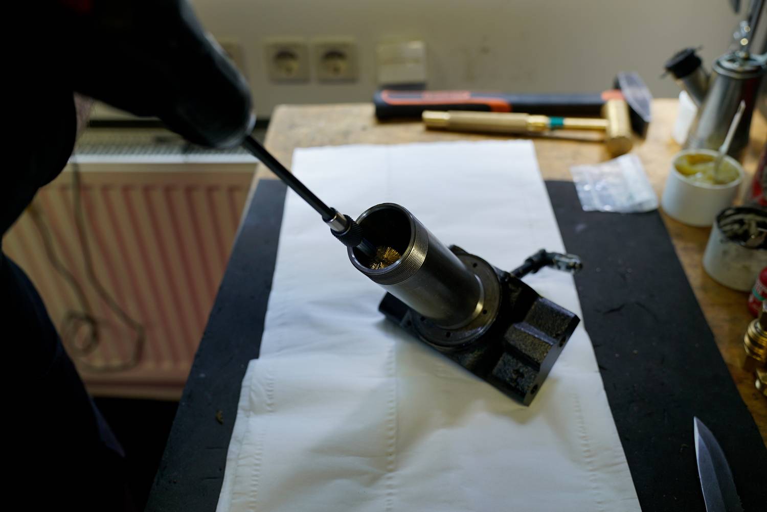 A person is working with a drill on a metal piece clamped in a vice on a workbench.