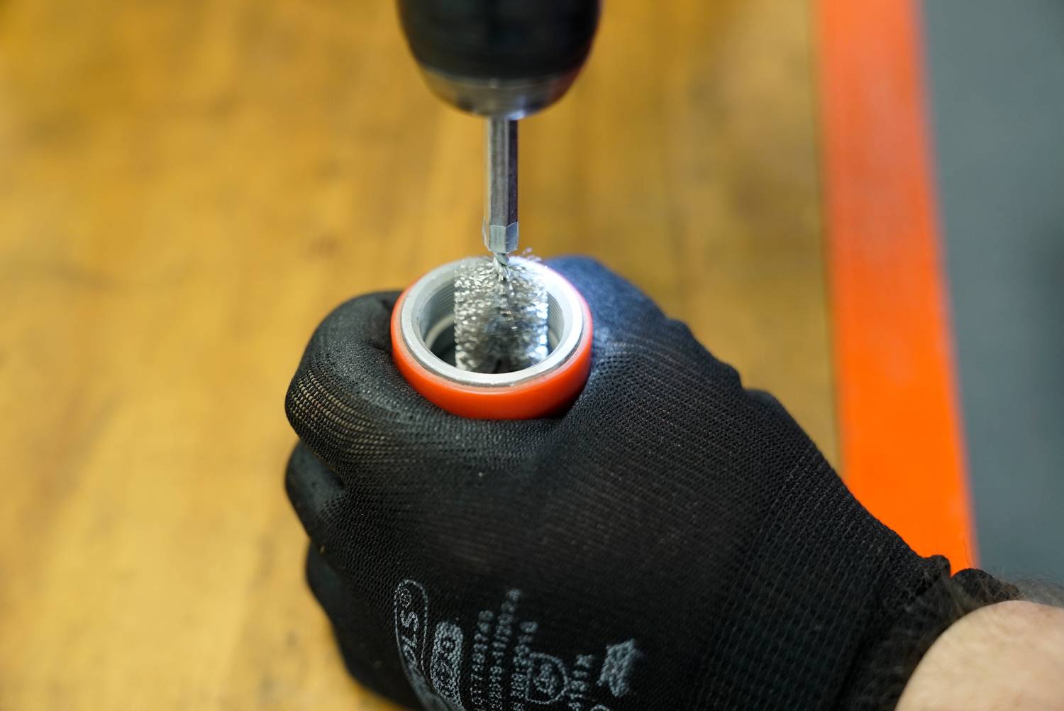 A person wearing a black glove is holding a metal sleeve while a drill is being inserted into the opening.