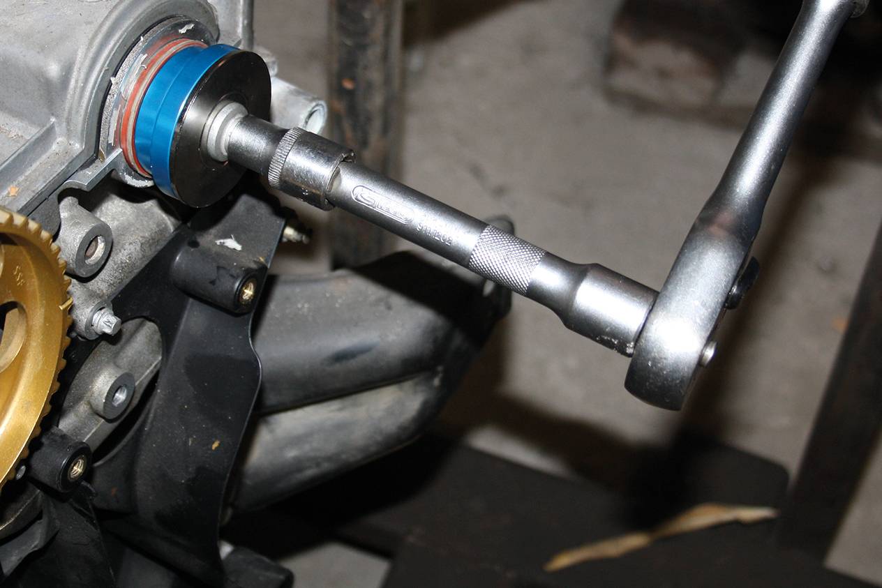 A ratchet is used to secure a screw on an engine. Motor components can be seen in the background.