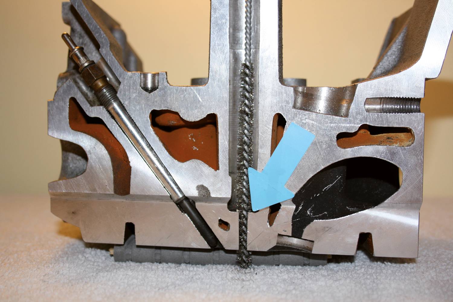 A metallic machine component in cross-section, showing the internal structure and a blue arrow pointing to a specific detail.