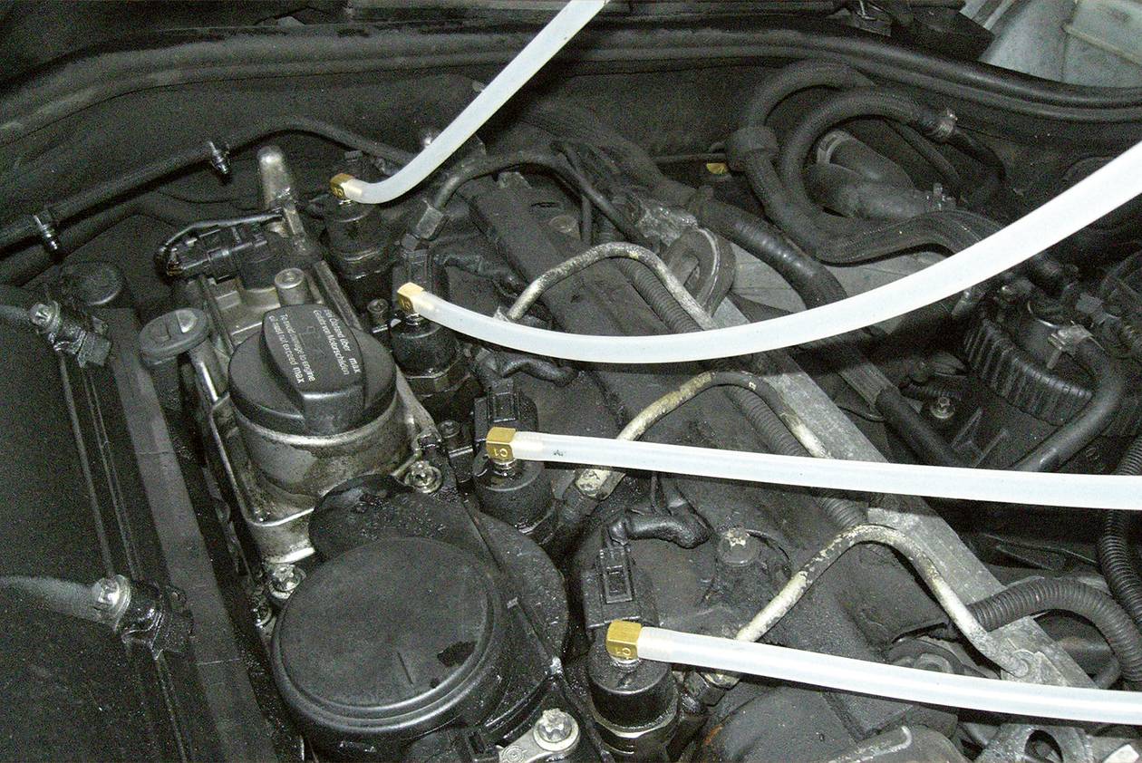 'Engine compartment of a vehicle; several transparent hoses are connected to the engine, presumably for maintenance or repair.'