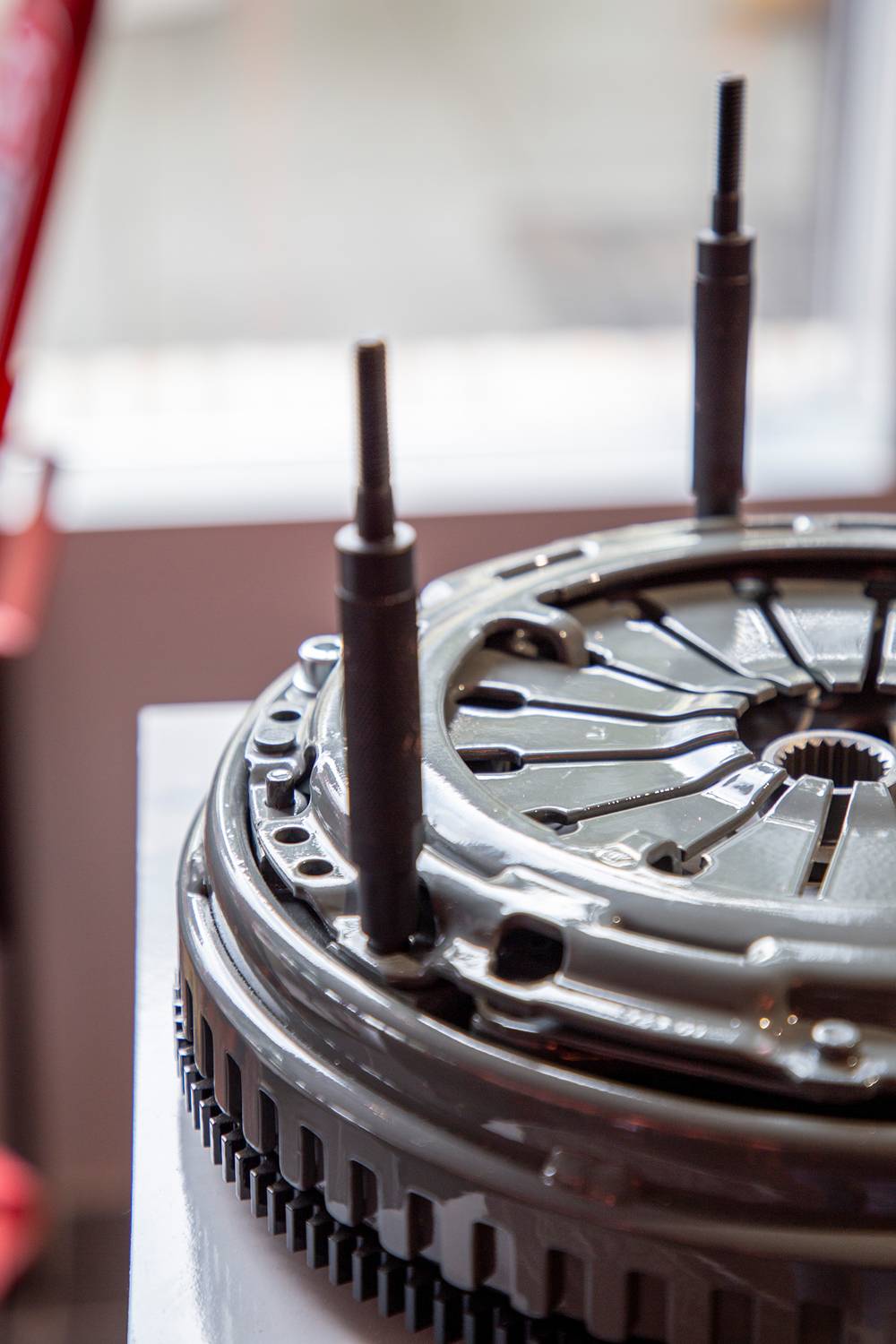 A close-up of a car part, likely a clutch disc, placed on a table. Metal rods are visible.