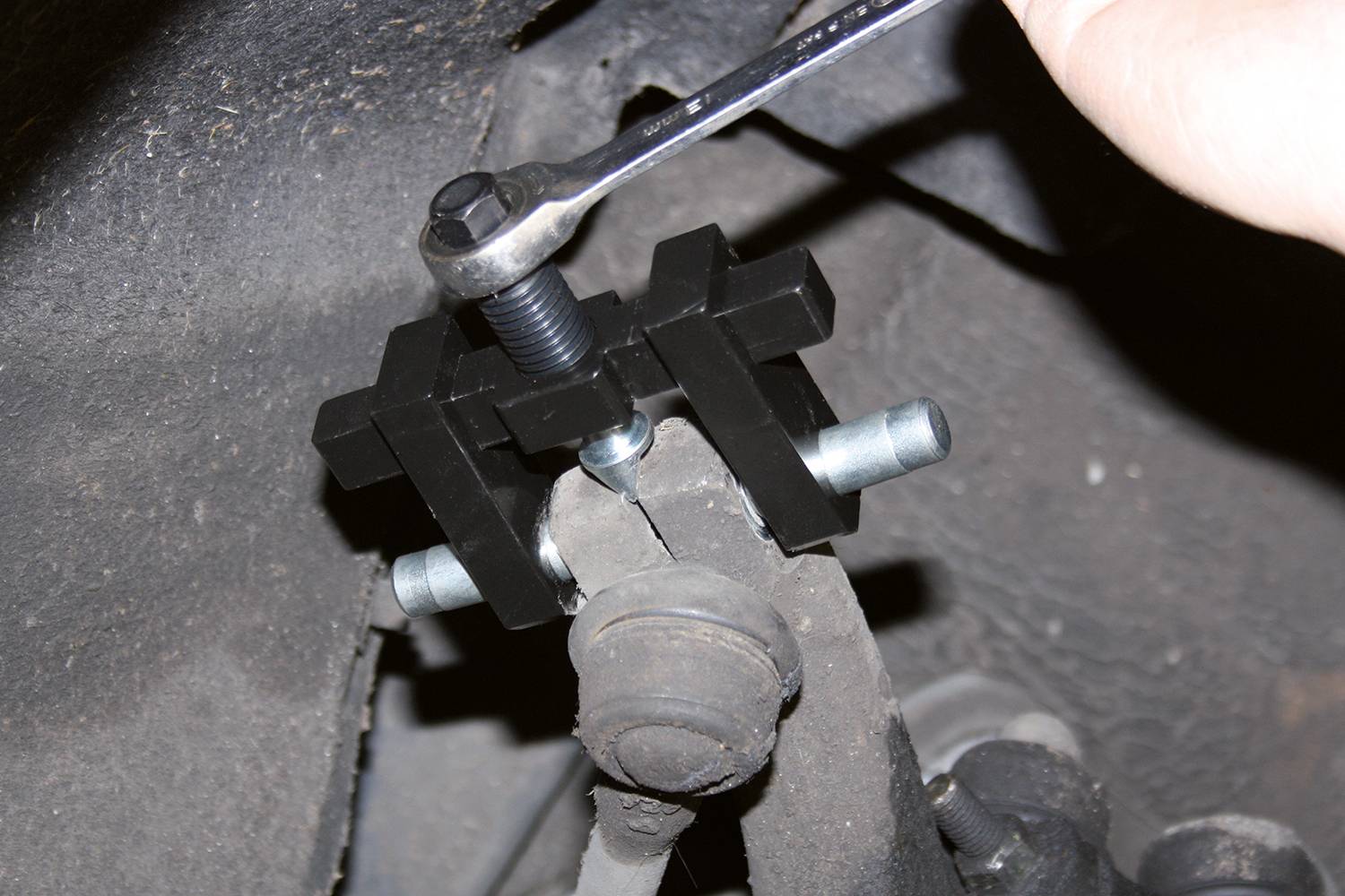 A hand is using a spanner to tighten an axle joint puller on a vehicle part.