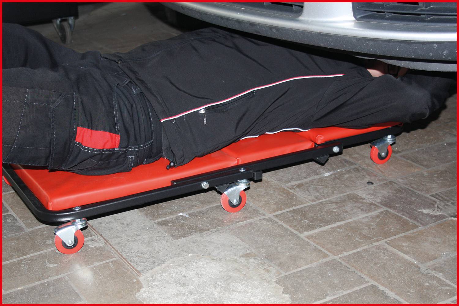 A mechanic is lying on a wheeled trolley underneath a vehicle to carry out repairs or inspections.