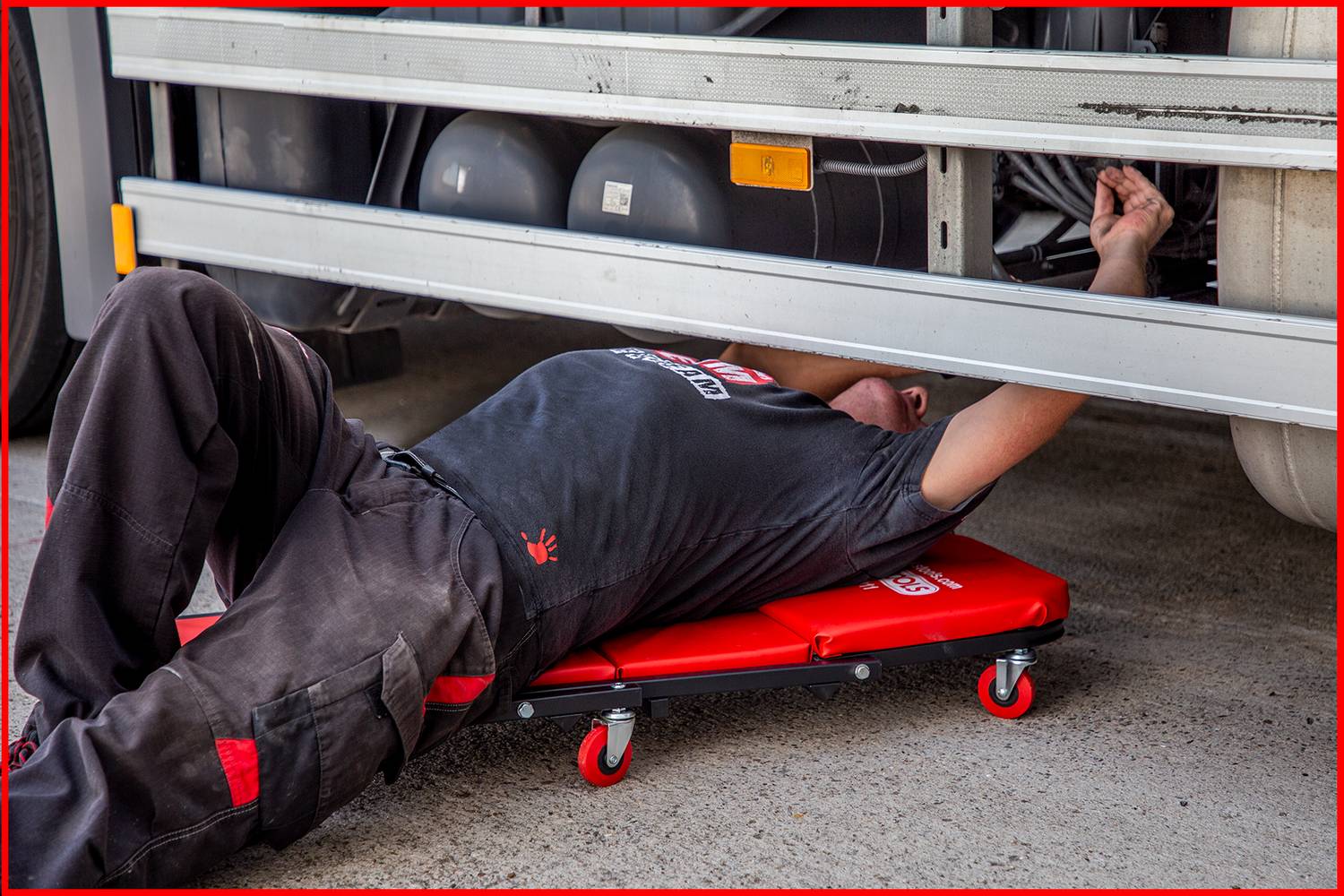 A person is lying on a trolley underneath a lorry and carrying out repairs. They are wearing workwear.