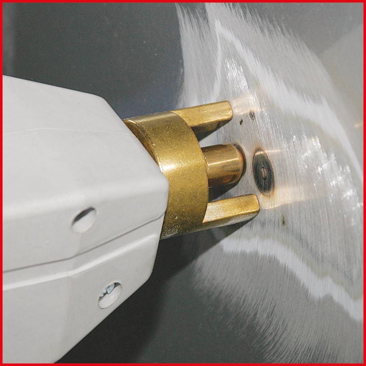 Close-up of a drill bit boring a hole into a metallic surface. Sparks are spraying from the opening.