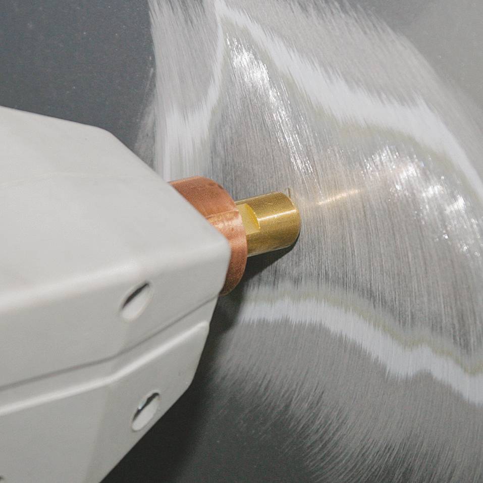 A device is polishing a metal surface. A rotating brush creates a glossy finish. A close-up shows details of the process.