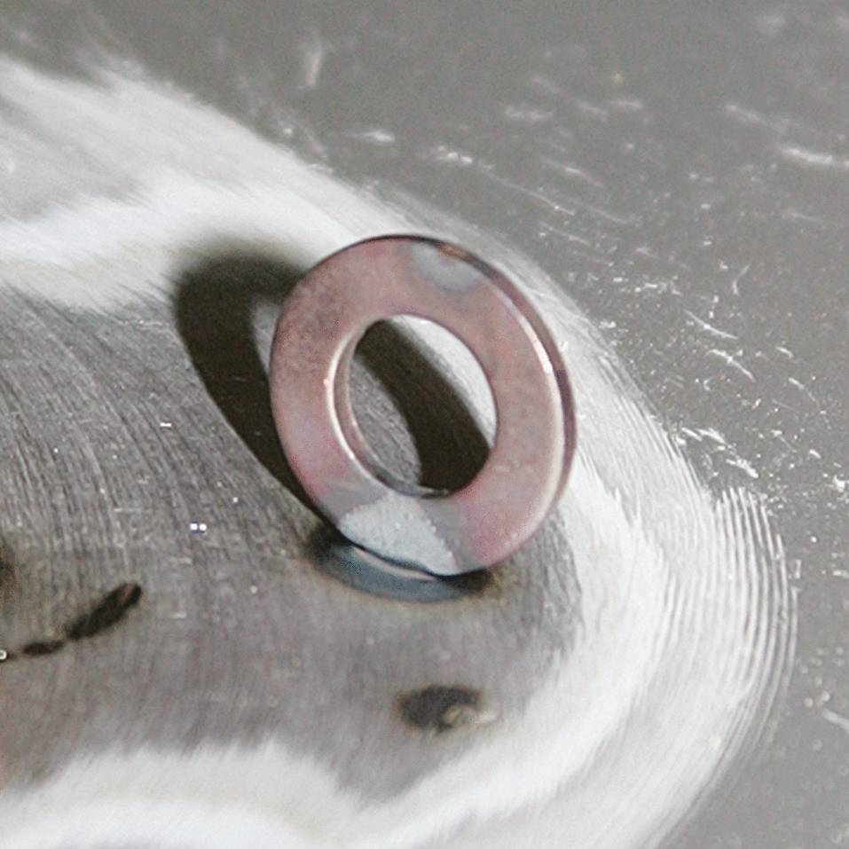 A pink washer lies at an angle on a metallic surface. It slightly reflects the light.
