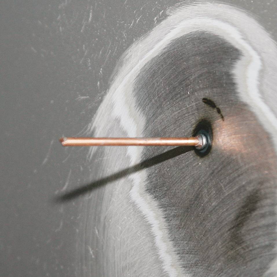 An electron beam strikes a metal surface and generates concentric circles representing interference patterns.