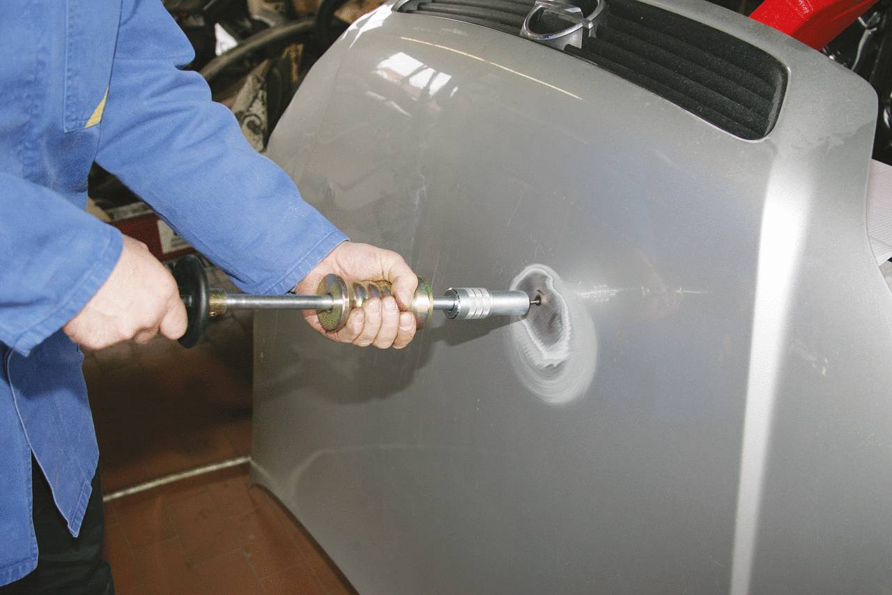 A person is repairing a car body by applying a dent removal technique. They are using a specialist tool to remove a dent.