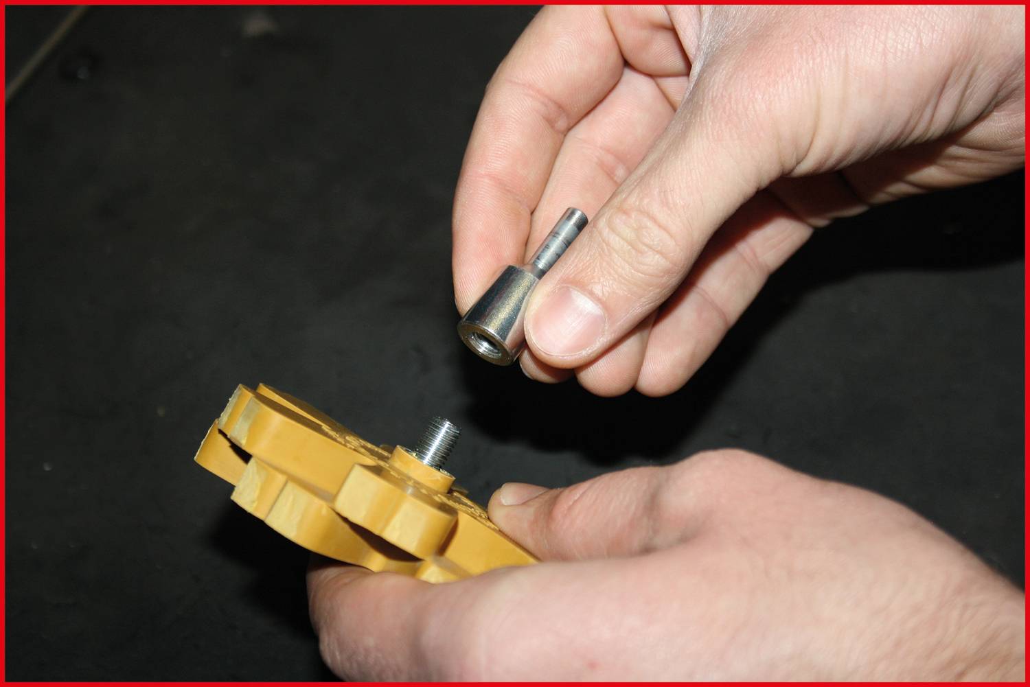 A person is mounting a metal part onto a yellow device. Hands are holding both parts that are being aligned with each other.