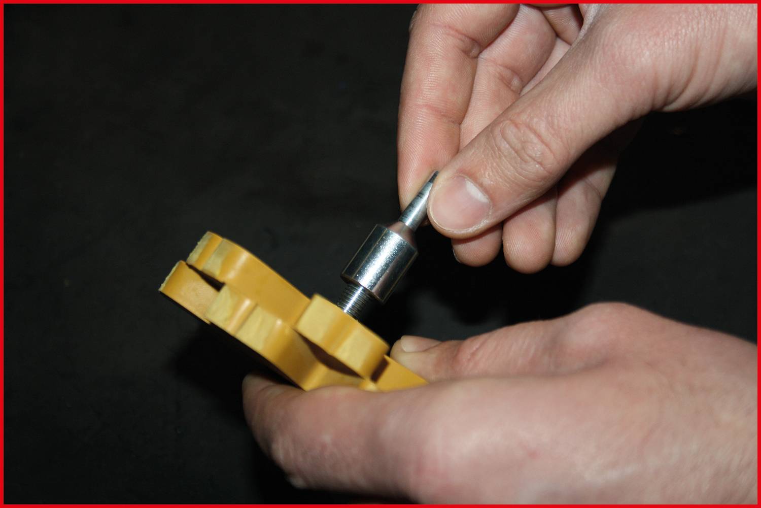 'A hand is holding a yellow piece of material, which is being worked on with a metal tool in the other hand.'