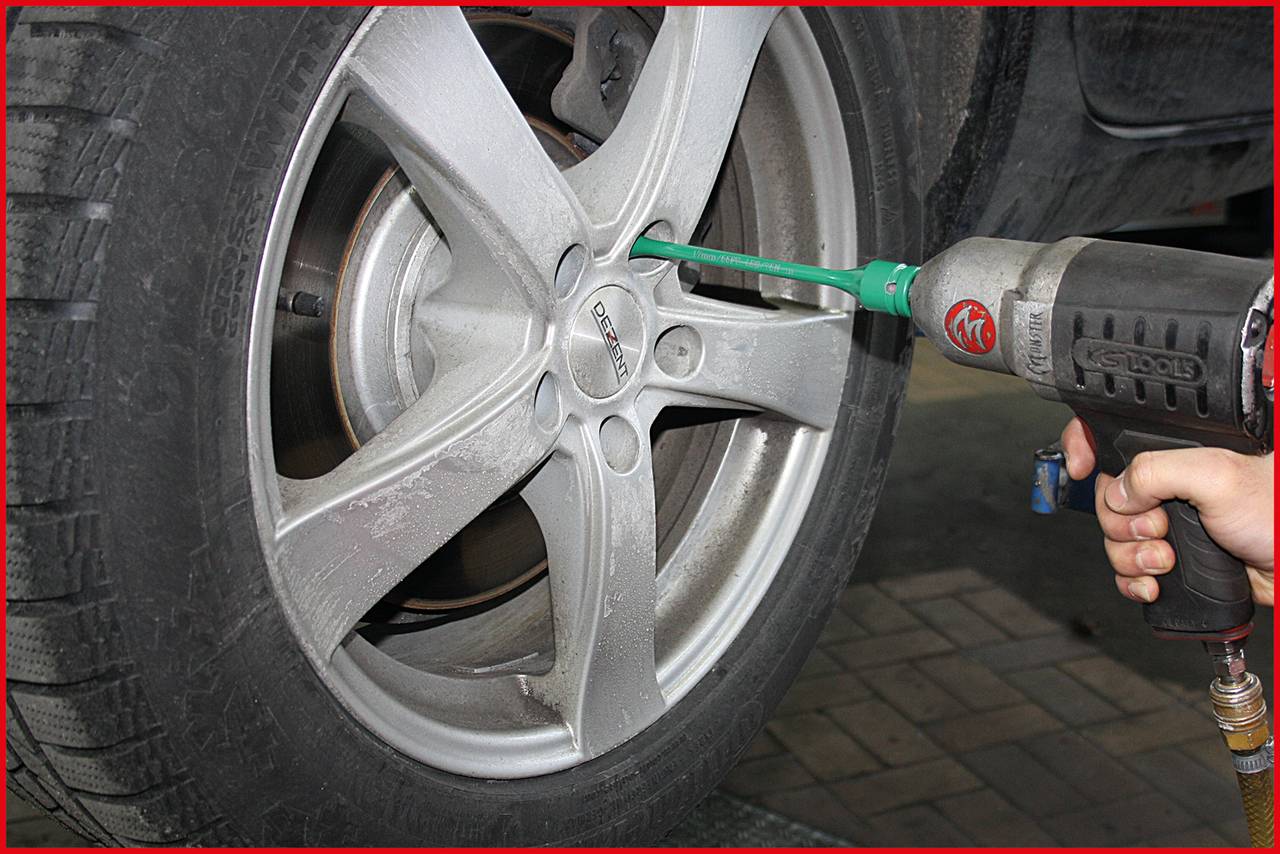 A person is using a spanner to tighten a wheel nut on a car tyre. The tyre is on a car lift.