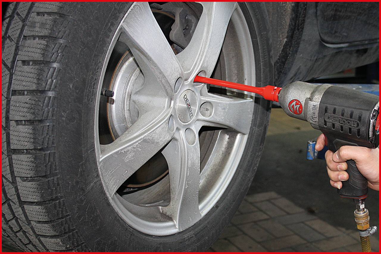 A person is changing a car tyre wheel with an impact driver. The focus is on the rim and the power tool.