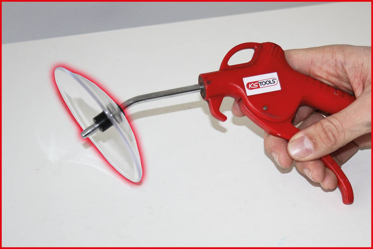 A red compressed air device is being held by a hand. It has a round disc and is likely used as a cleaning aid.