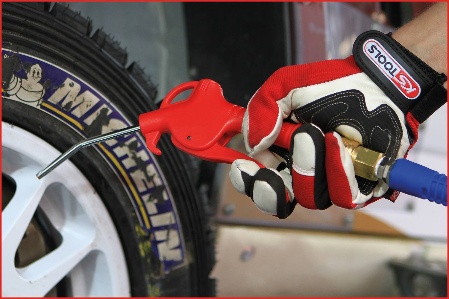 A hand wearing a red and white glove is holding an air pump close to a Michelin-branded tyre.