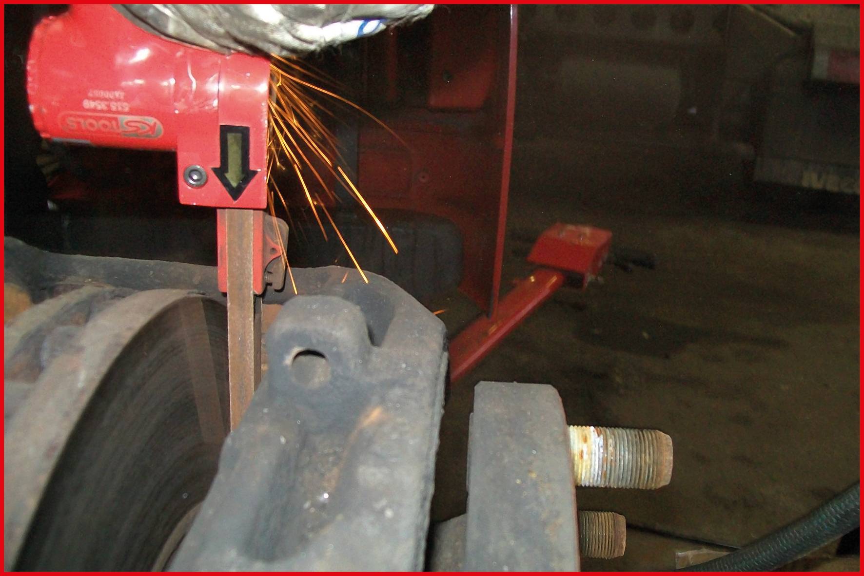 A red-rimmed grinding tool removes material with a shower of sparks from a metal piece in a workshop environment.