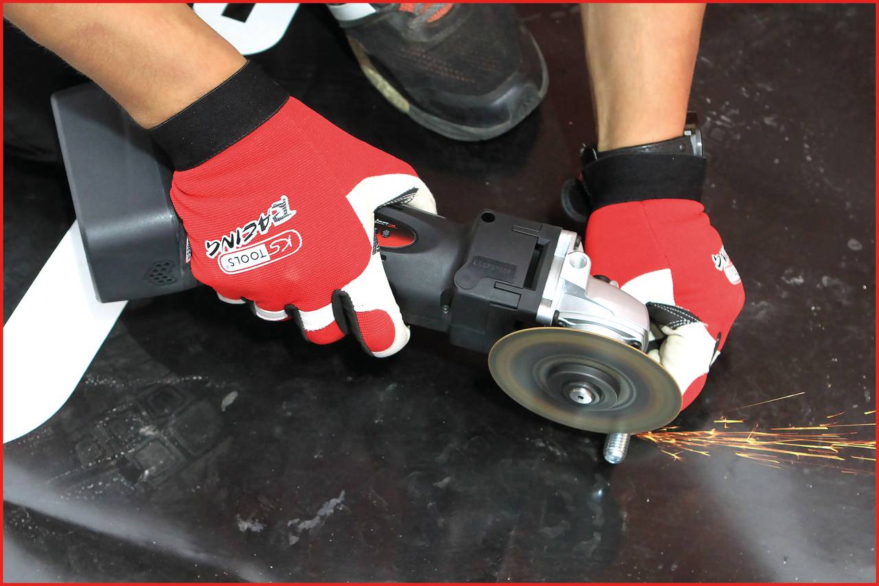 A person is grinding metal with an angle grinder. Sparks are flying. The person is wearing red protective gloves.