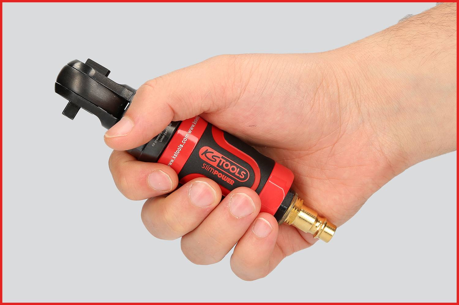 A hand is holding a red tool with a black handle. The tool appears compact and could be an impact driver.