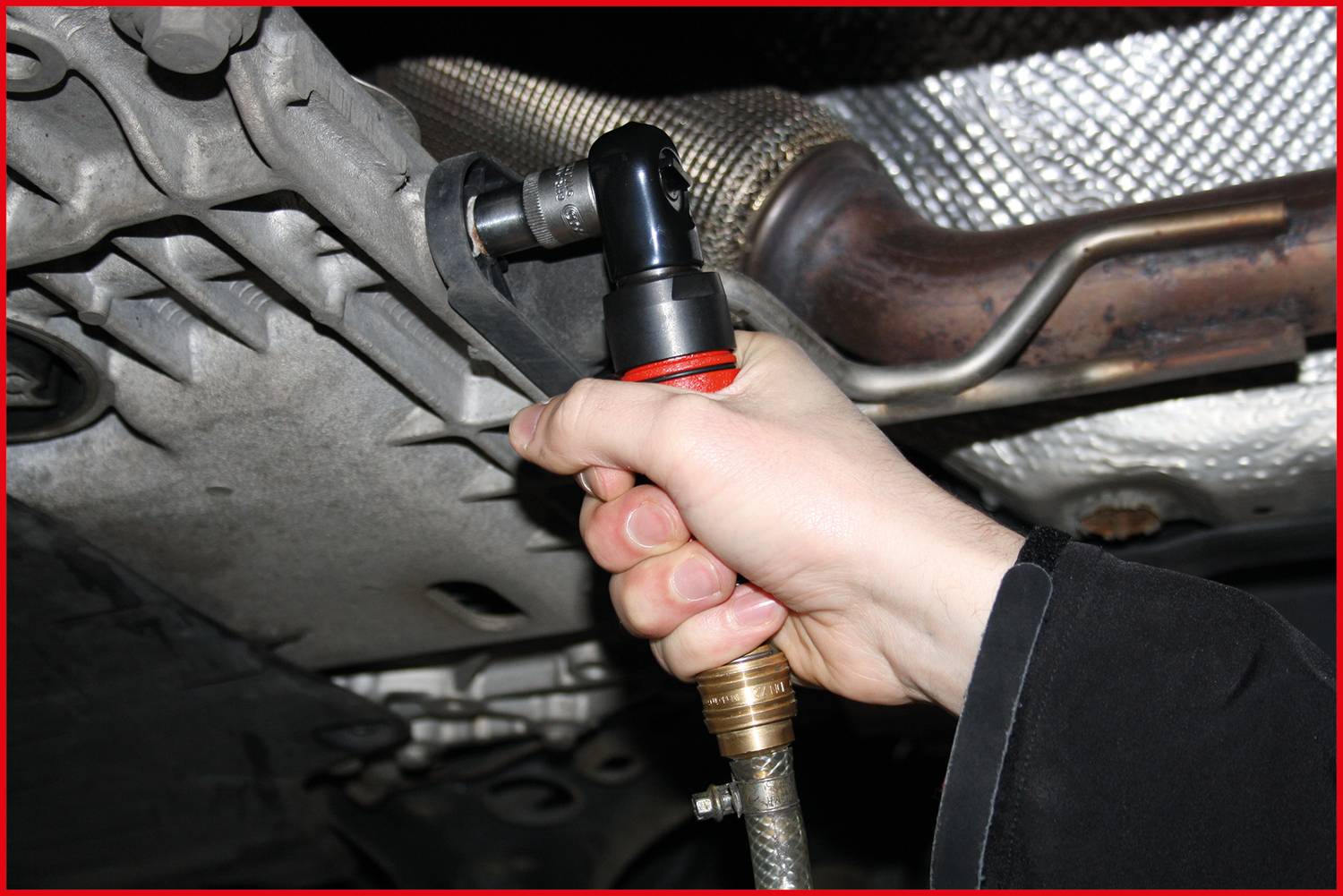 A person is using a pneumatic tool to tighten a screw at the underside of a vehicle.