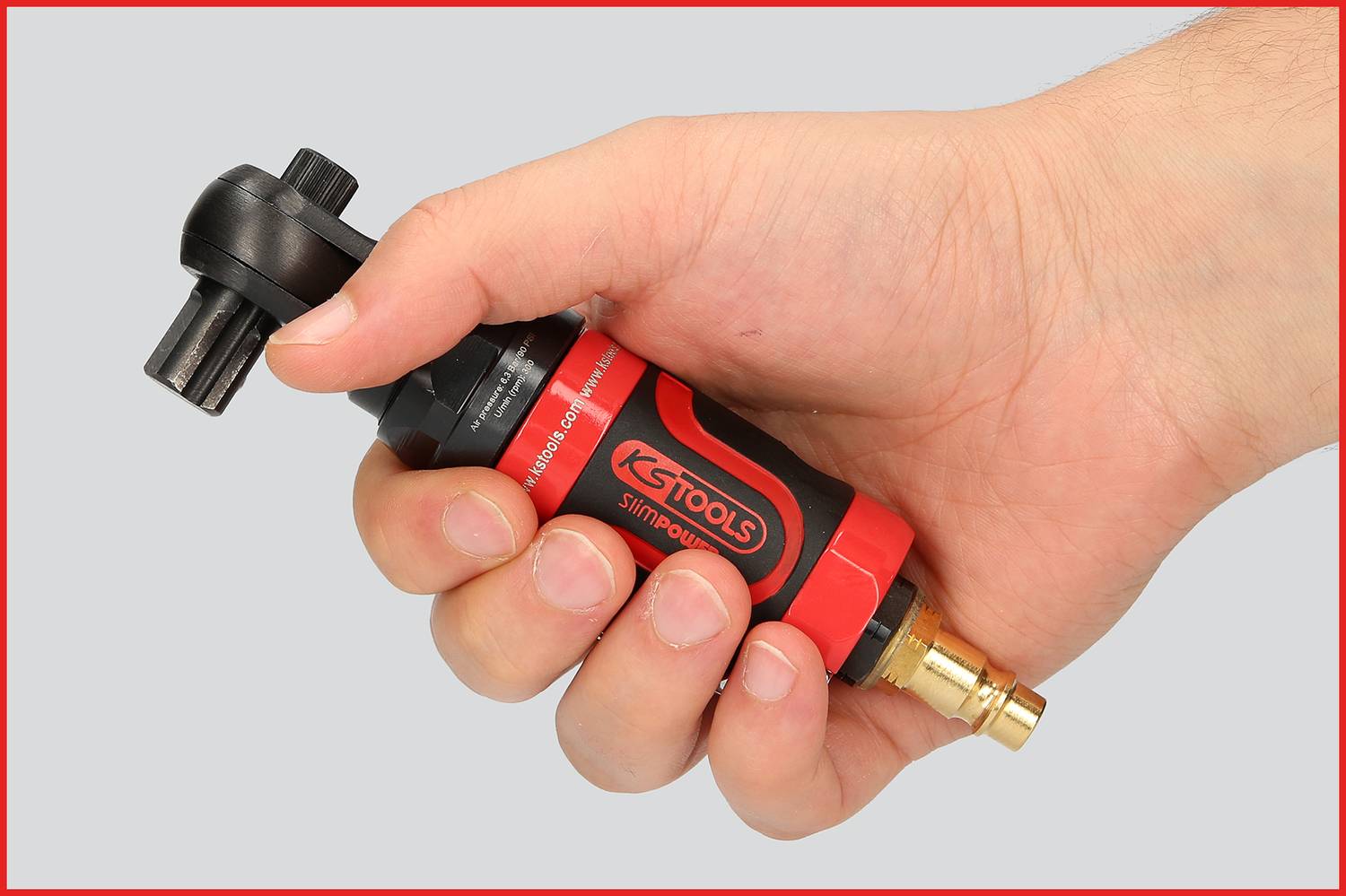 A hand is holding a red and black tool. It is a pneumatic angle grinder with a metal connector.