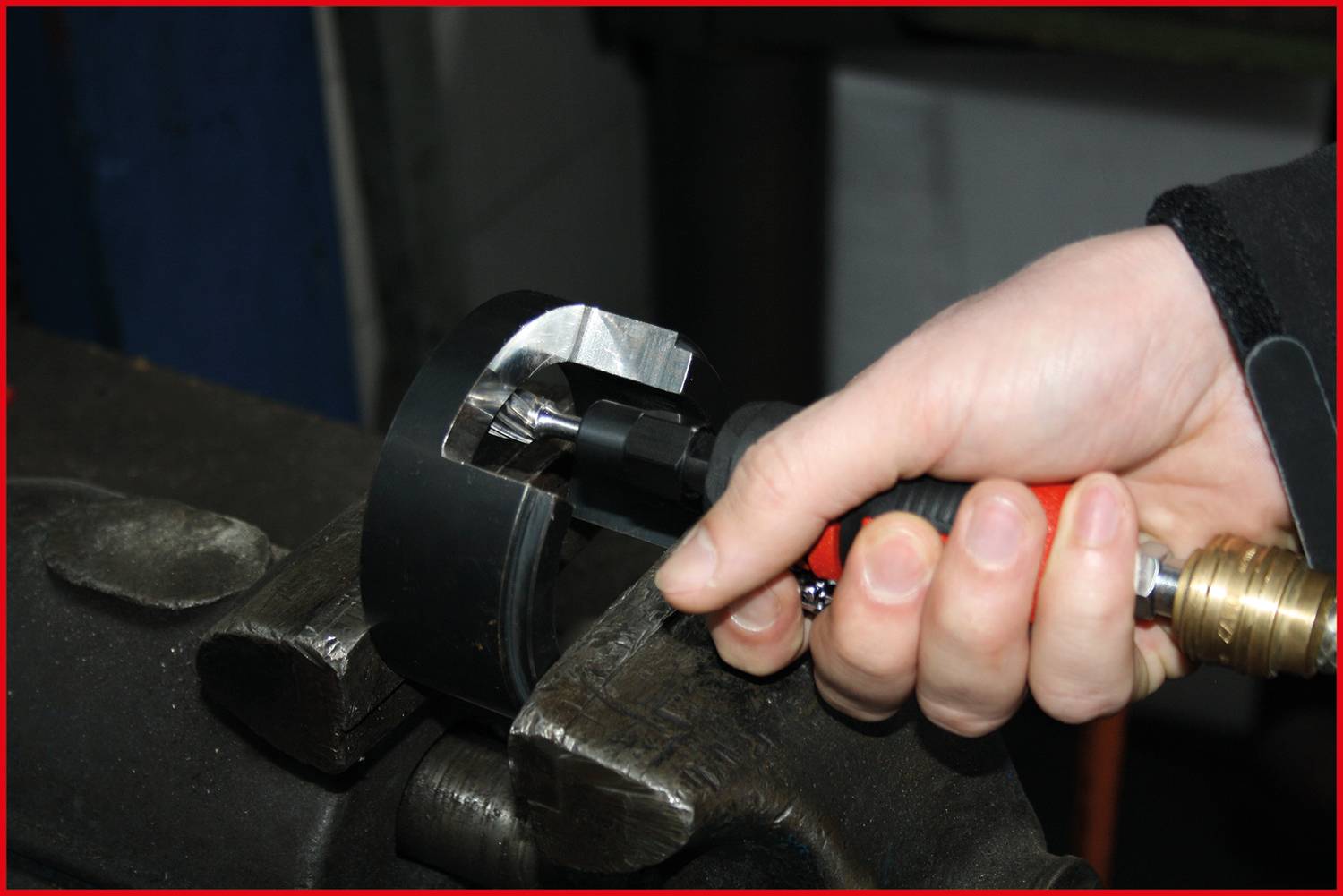 A hand holds a torque tool that is applied to a metal piece in a vice to process or tighten it.