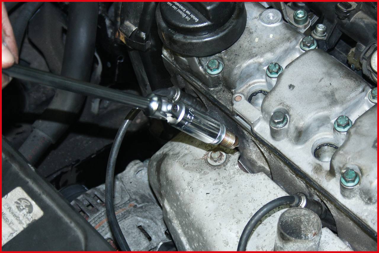 A hand is using a test probe to check for a spark at a spark plug terminal of an engine.