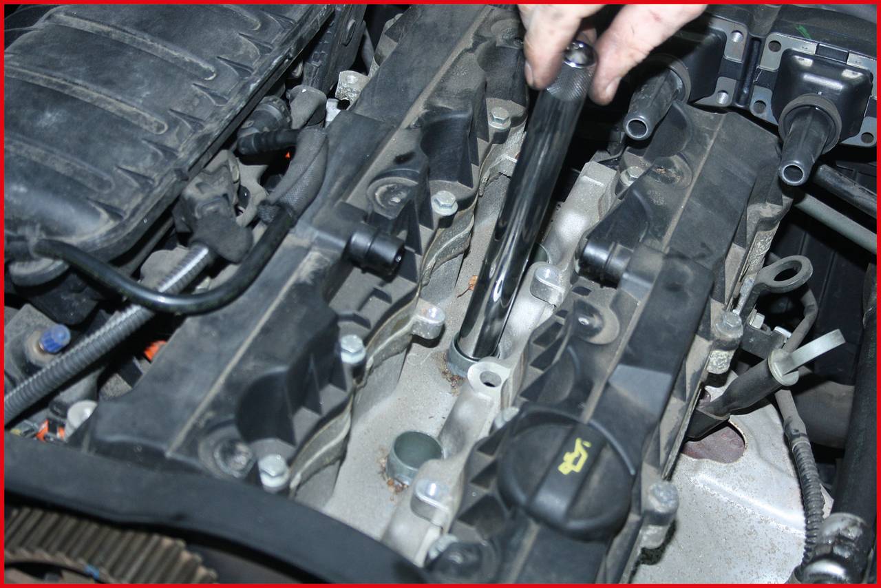 'A person is repairing a car engine, holding a tool over the cylinder head. Various engine components are visible in close proximity.'