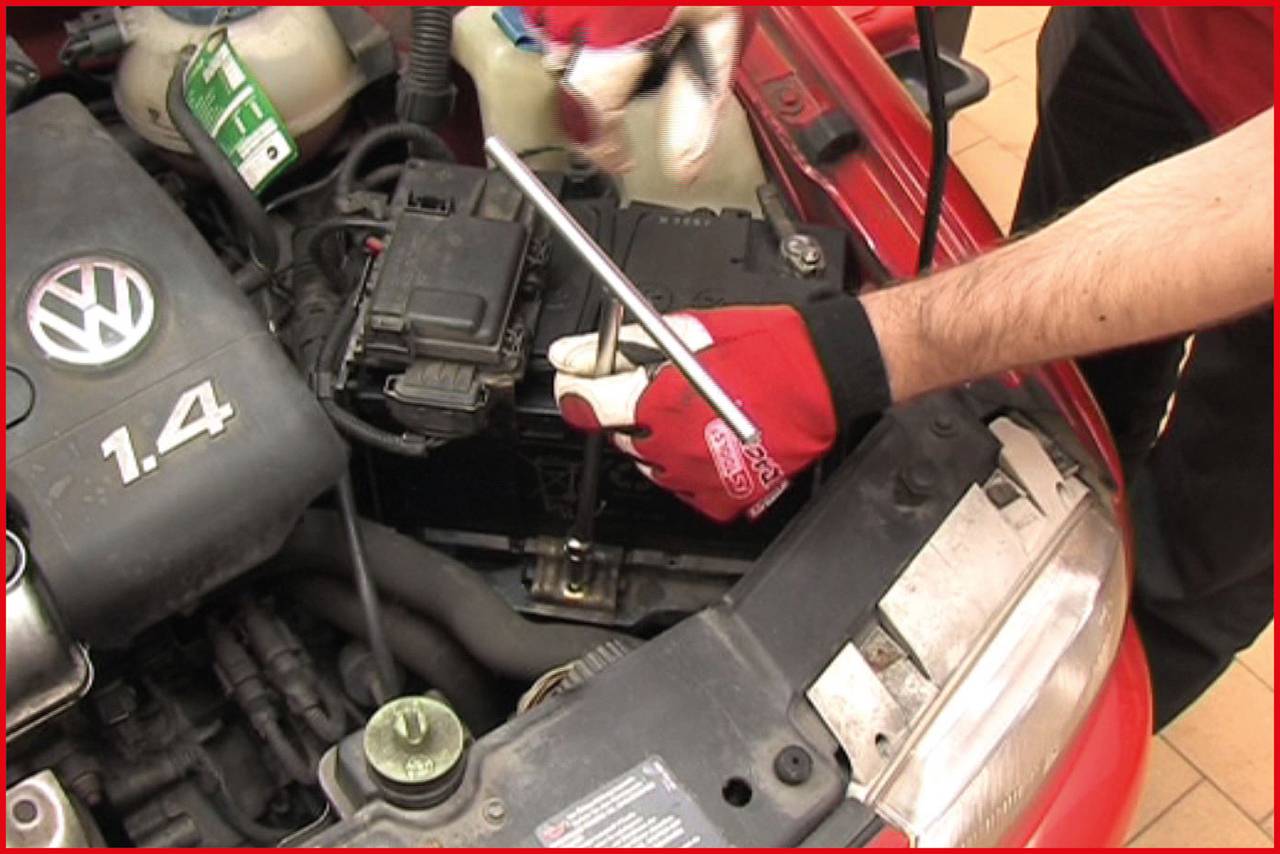 A person wearing red gloves is carrying out maintenance work on a car engine bay, focusing on a screw connection.