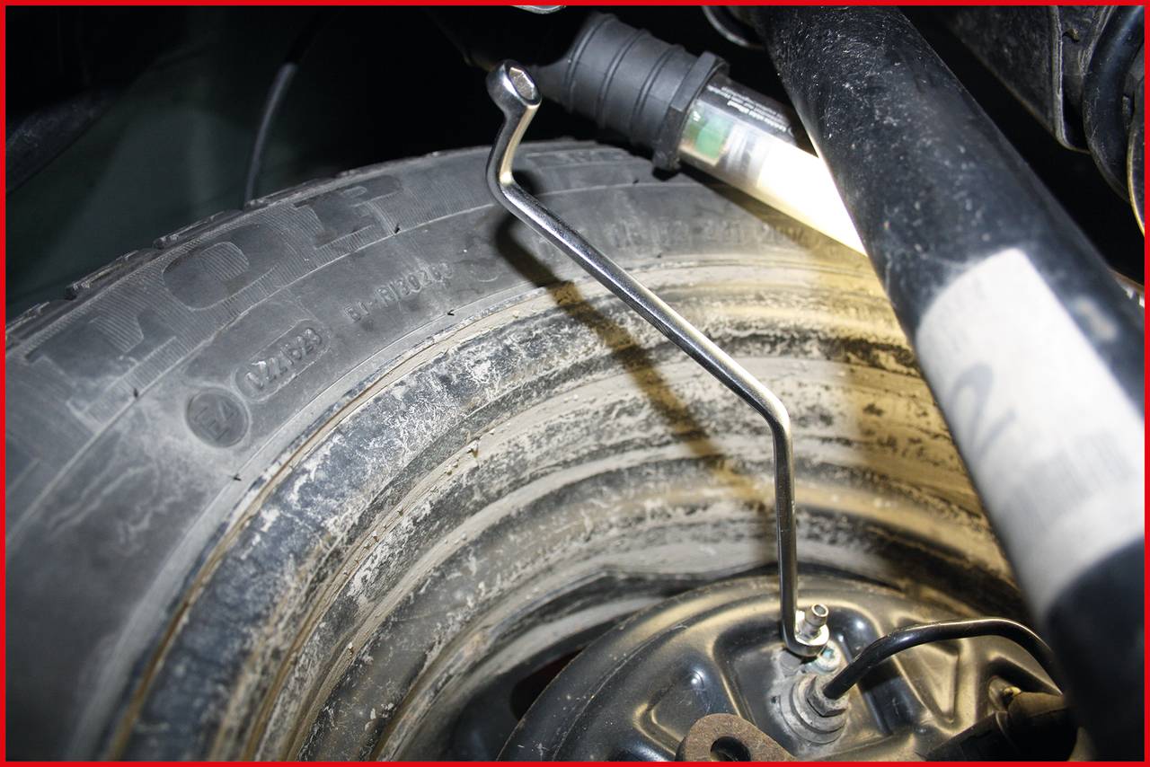 A spare tyre is being mounted in a vehicle. A lamp illuminates the area, while a tool secures the wheel.