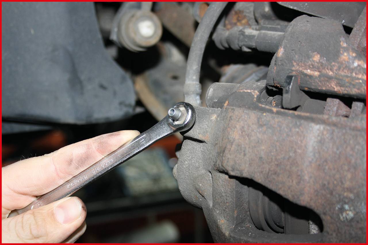 'A hand holds a spanner, tightening a screw on some rusty car parts. Vehicle maintenance is being carried out.'
