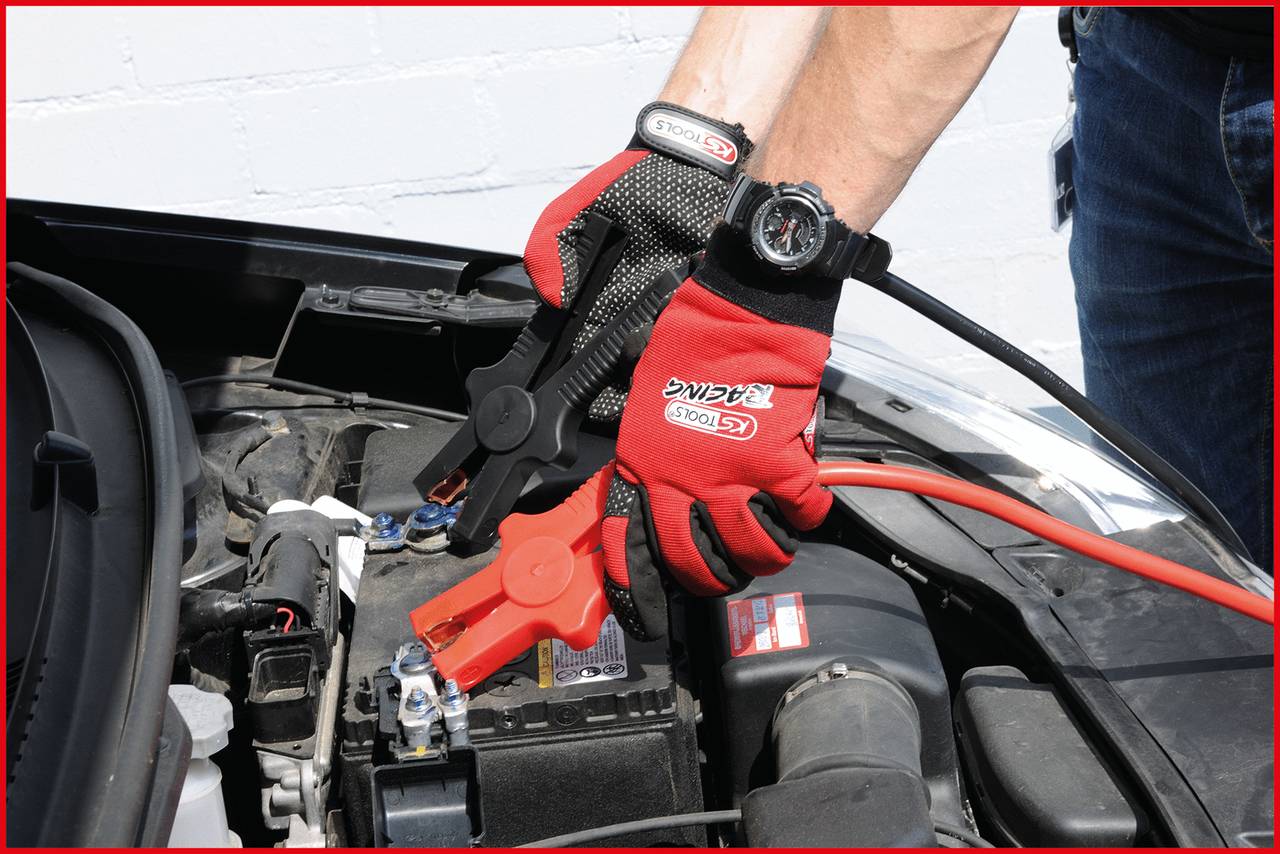 A person wearing red gloves is connecting a red jump lead to a car battery in order to start the vehicle.